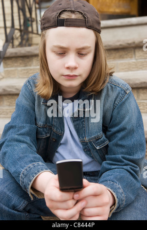 Caucasian boy sitting on steps text messaging on cell phone Stock Photo