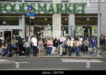 People wait at a crosstown bus stop on 14th Street across from Union Square in New York City. Stock Photo