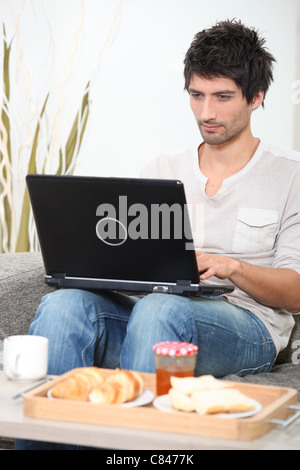Man having breakfast whilst using laptop Stock Photo