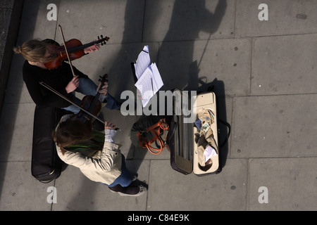Looking down on two young women playing violins for money on the embankment of the River Thames, London Stock Photo