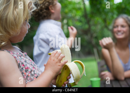 Little girl outdoors with her family, eating banana Stock Photo