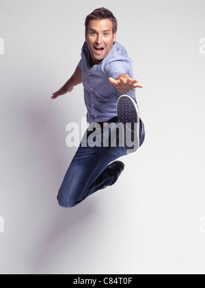 Happy jumping young man wearing jeans and a shirt isolated on gray background. The image has a very slight motion blur. Stock Photo