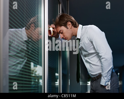 young adult italian business man banging his head against a window in office. Horizontal shape, copy space