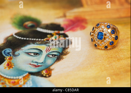 Indian Blue sapphire and diamond gold ring on a Traditional Indian oil painting of Lord Krishna Stock Photo