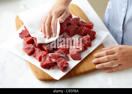 Woman using Paper Towel to dry Beef Cubes Stock Photo