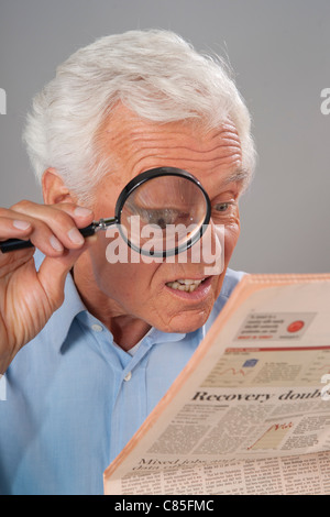 Man Looking at Newspaper with Magnifying Glass Stock Photo