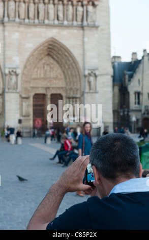 A tourist taking a photo of his wife in front of Notre Dame in Paris, France Stock Photo