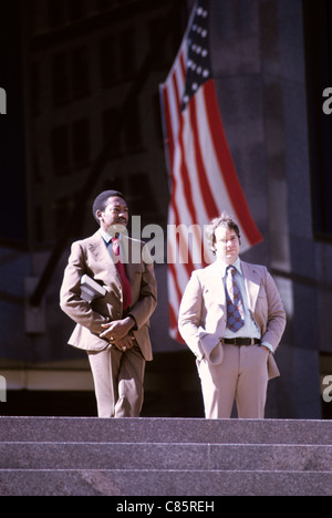 two multi- racial businessmen talk on steps of Bank of America in san francisco  with American flag in background Stock Photo