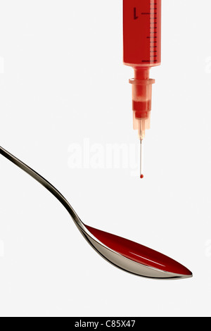 Syringe filled with red liquid and spoon on white background