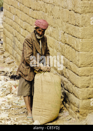 Full-length portrait of a Yemini man wearing a red and white checked keffiyeh and holding a burlap bag, Thula, Yemen Stock Photo