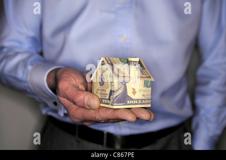 Man holding model house folded with dollar bill, mid section Stock Photo