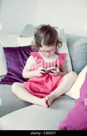 Little girl sitting on couch looking at picture on cell phone Stock Photo