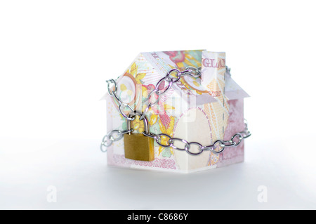 Model house folded with British pound banknotes chained and padlocked Stock Photo