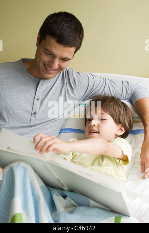 Father and son reading book together in bed Stock Photo