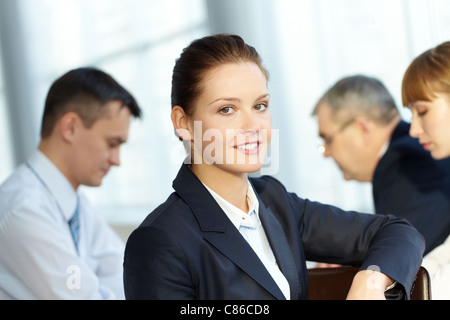 A young businesswoman smiling against working colleagues Stock Photo