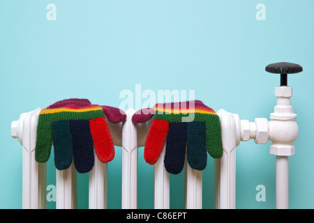 Photo of a pair of hand knitted striped woolen gloves drying on an old traditional cast iron radiator. Stock Photo