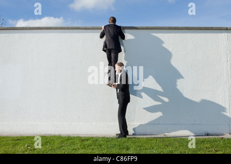 Businessman lifting colleague over wall Stock Photo