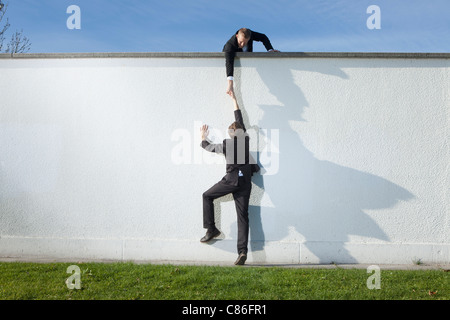 Businessman pulling colleague over wall Stock Photo