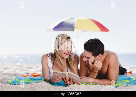 Couple reading book together on beach Stock Photo