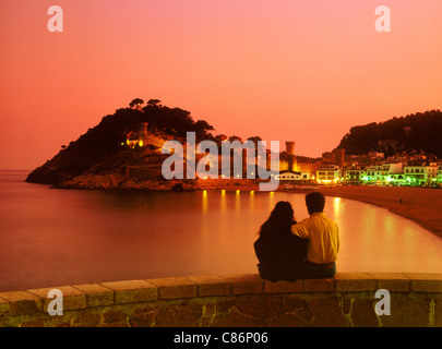 Couple sitting on wall looking at Tossa de Mar Castle at sunset in Girona Province of Spain Stock Photo