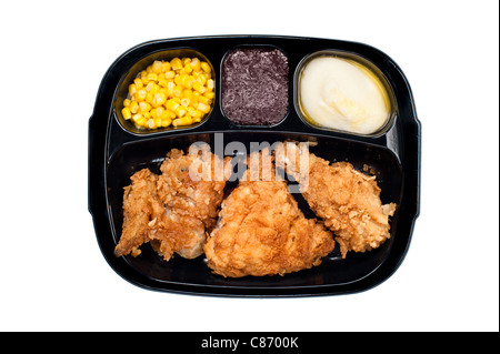 A cooked tv dinner of fried chicken, corn, mashed potatoes and dessert in a plastic black tray. Stock Photo