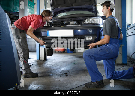 Germany, Ebenhausen, Mechatronic Technicians carrying car in repair garage Stock Photo