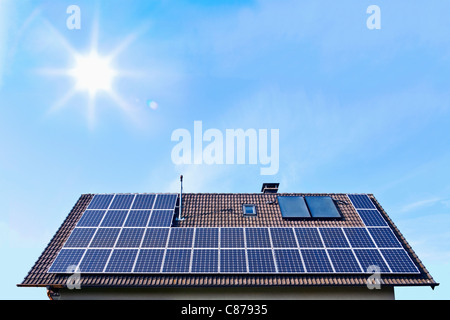 Germany, Solar panels on houseroof in front of blue sky with sun Stock Photo