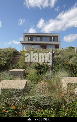 Modern beach house, against blue sky, with grasses and sea defense in foreground, Thorpeness beach, Suffolk Heritage Coast, UK. Stock Photo