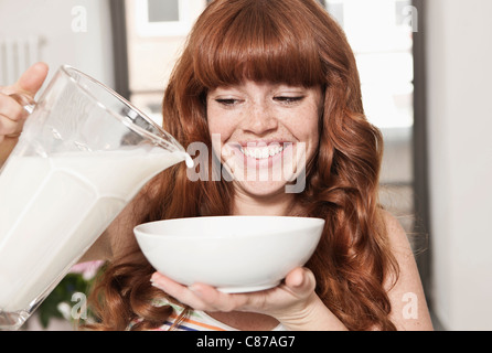 Germany, Berlin, Close up of young woman preparing cereals, smiling