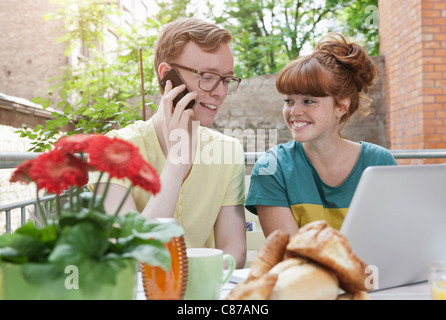 Germany, Berlin, Young couple using cell phone and laptop, smiling Stock Photo