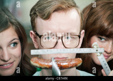Germany, Berlin, Close up of young man measuring grilled sausage and women beside him, smiling Stock Photo
