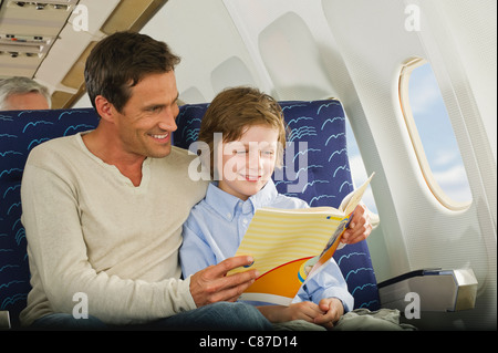 Germany, Munich, Bavaria, Man and boy reading book in economy class airliner Stock Photo