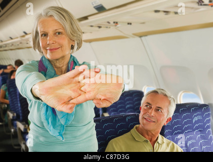 Germany, Munich, Bavaria, Senior woman stretching and man looking in economy class airliner Stock Photo