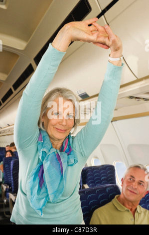 Germany, Munich, Bavaria, Senior woman stretching and man looking in economy class airliner Stock Photo