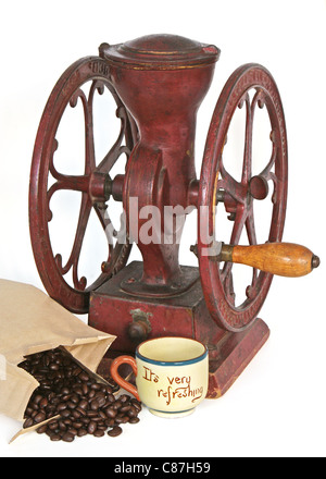 Antique red wheel coffee grinder with wood handle near some whole beans and an empty cup. Stock Photo