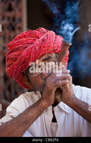 Indian man wearing Rajasthani turban smokes traditional clay pipe in Narlai village in Rajasthan, Northern India Stock Photo