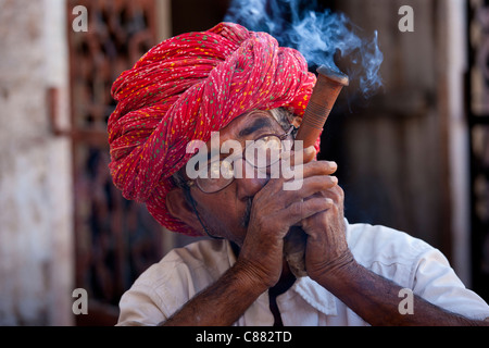 Indian man wearing Rajasthani turban smokes traditional clay pipe in Narlai village in Rajasthan, Northern India Stock Photo