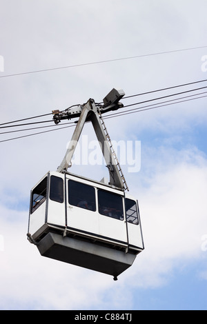Cable Car on wires over cloudy sky with non-recognisable silhouettes of people inside. Stock Photo
