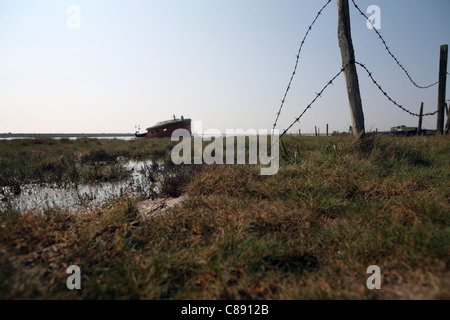 River Ore / Alde, bank / wall at Orford Suffolk, UK showing abandoned boats in background Stock Photo