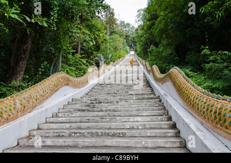 Novice monk in golden robe hikes up an extremely long staircase up a hill at Wat Doi Saket in northern Thailand Stock Photo