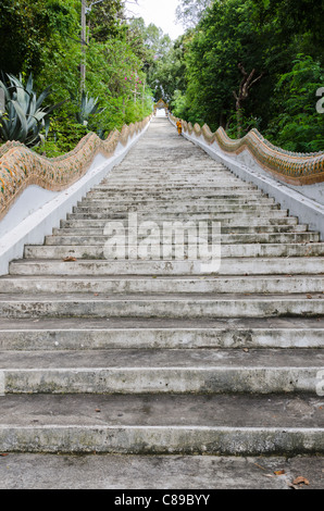 Novice monk in golden robe hikes up an extremely long staircase up a hill at Wat Doi Saket in northern Thailand Stock Photo