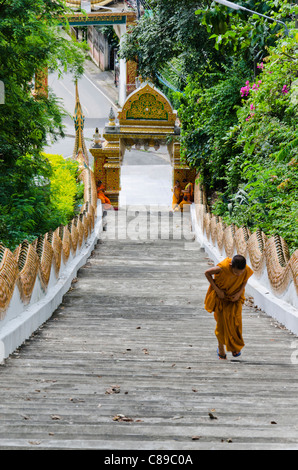 Novice monk in golden robe hikes up an extremely long staircase up a hill at Wat Doi Saket in northern Thailand Stock Photo