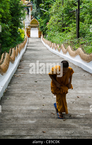 Novice monk in golden robe hikes up an extremely long staircase up a hill at Wat Doi Saket in northern Thailand Stock Photo