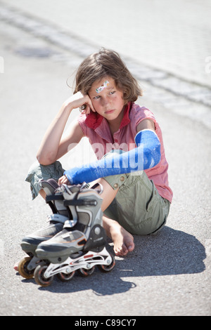 Germany, Bavaria, Wounded girl sitting on road after inline-skating accident Stock Photo