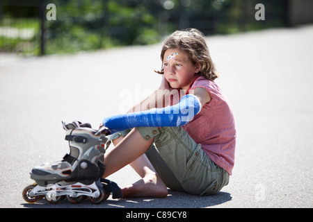 Germany, Bavaria, Wounded girl sitting on road after inline-skating accident Stock Photo