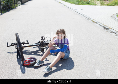 Germany, Bavaria, Wounded girl sitting on road after bicycle accident Stock Photo