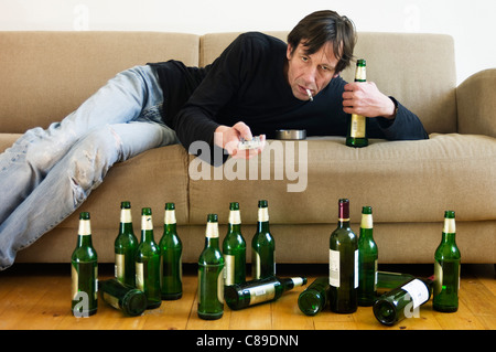 Germany, Hessen, Frankfurt, Drunk man lying on sofa with empty beer bottles Stock Photo