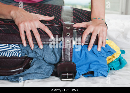 Italy, Tuscany, Young woman pushing stuffed suitcase in hotel room Stock Photo