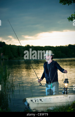 Germany, Bavaria, Woerthsee, Man with lantern fishing in boat at dusk Stock Photo