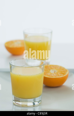 Glasses of orange juice with half oranges on table Stock Photo